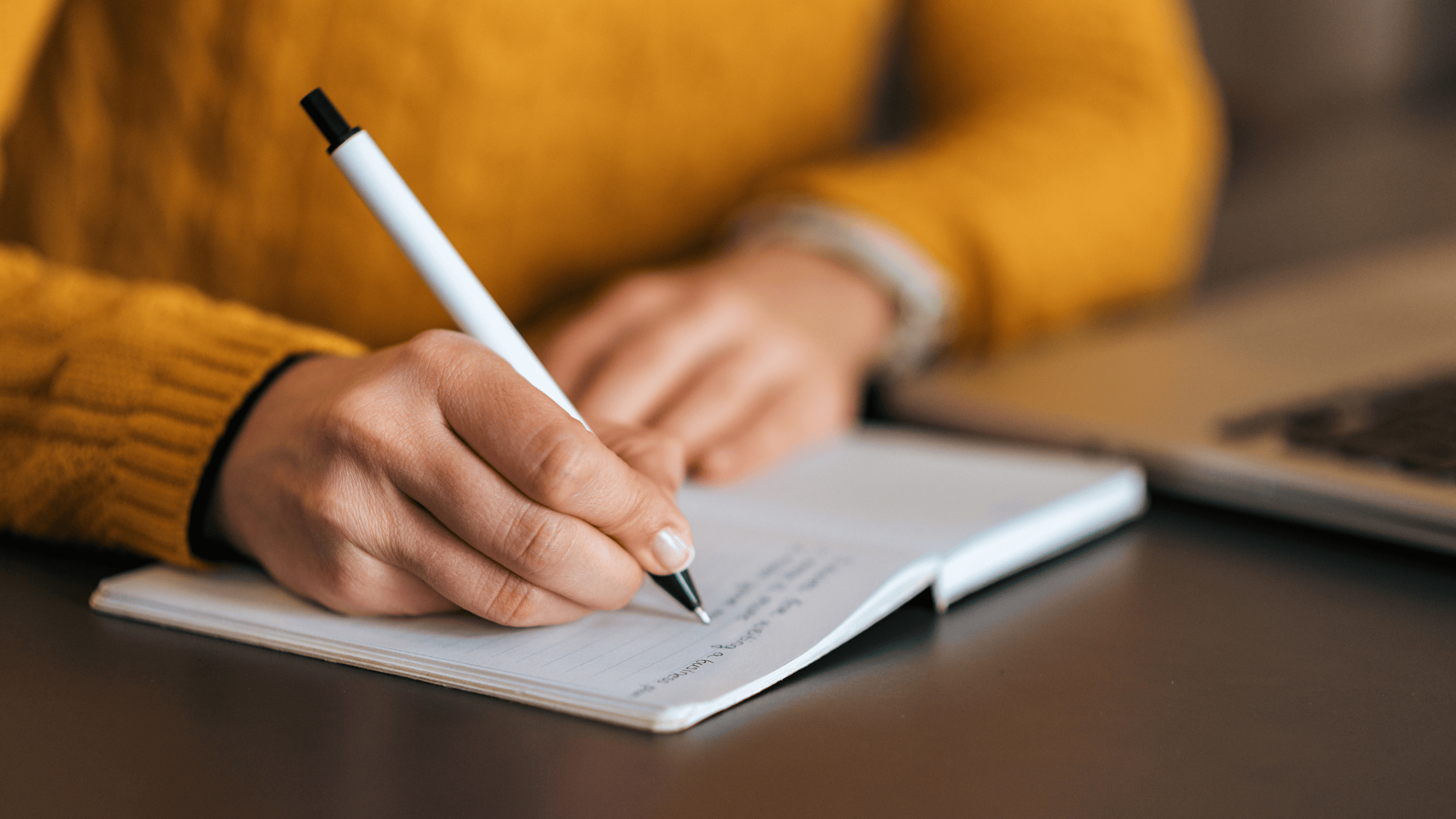 Person in yellow sweater writing in notebook.