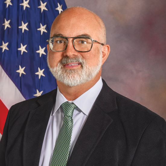 Lance Hampton, posing for a headshot in front of the American flag.
