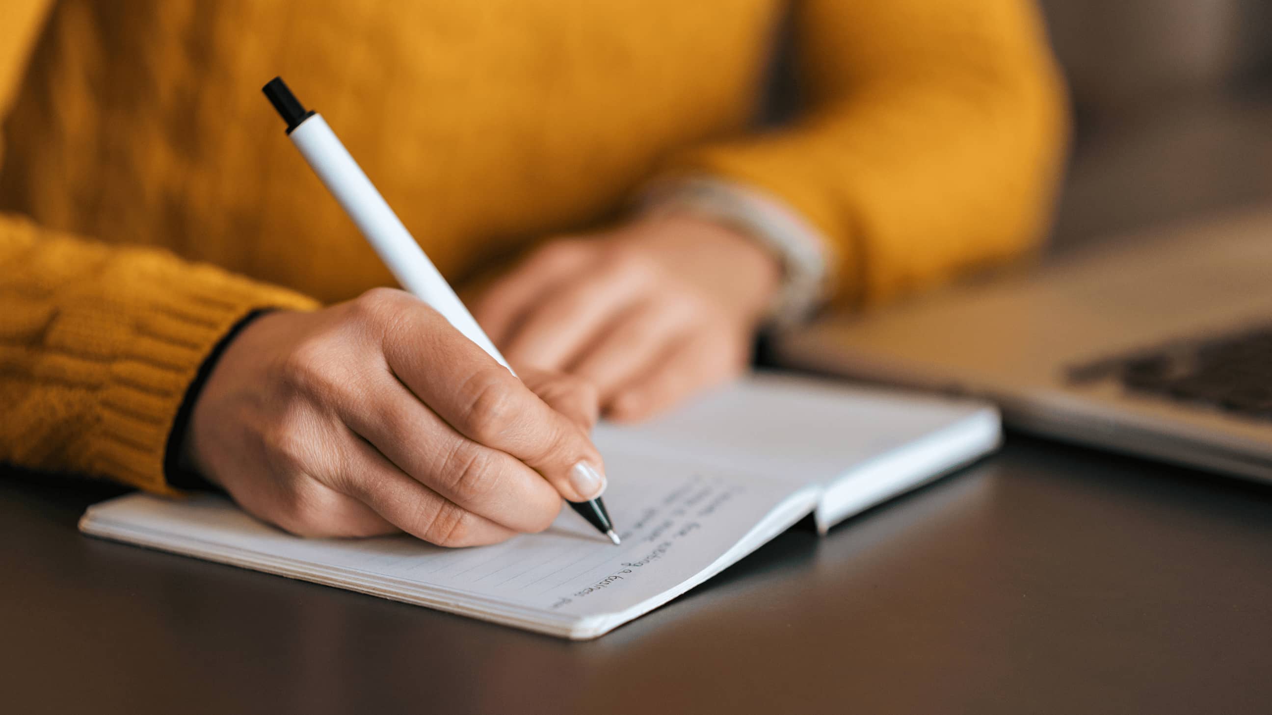 Person in yellow sweater writing in notebook.