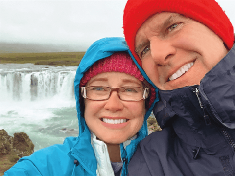 Charlotte Beyer Hubbell and Fred Hubbell stand in front of a waterfall