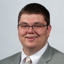 Elijah Redington smiles for a headshot against a light gray backdrop.