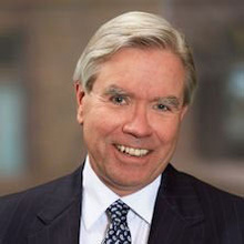 John Knapp smiles for a photo in a black suit.