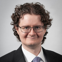 Ian Grunig smiles for a professional photo against a light gray backdrop.