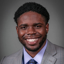 Alan Julien smiles for a professional photo against a dark gray backdrop.