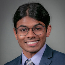 Adarsh Sukumar smiles for a professional photo against a dark gray backdrop.