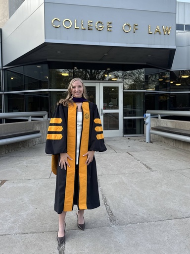 JoAnna Voss stands in front of the Boyd Law Building, posing for a photo in her commencement regalia.