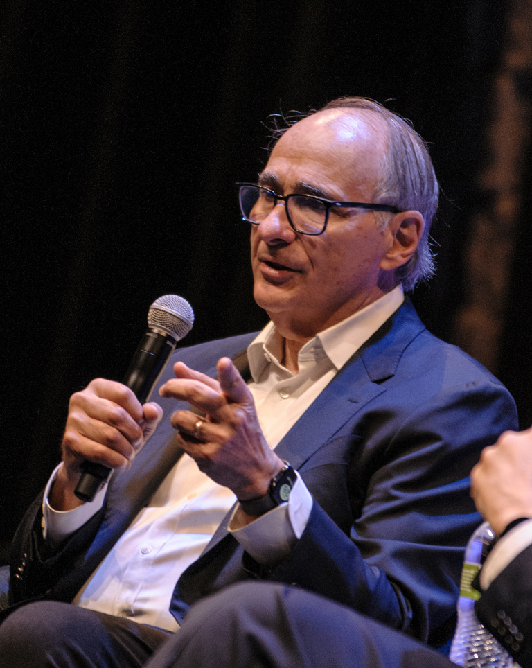 Axelrod speaks into a microphone to dinner attendees.