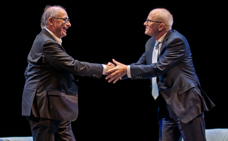 David Axelrod and Ben Kieffer shake hands on stage before the beginning of the lecture. 