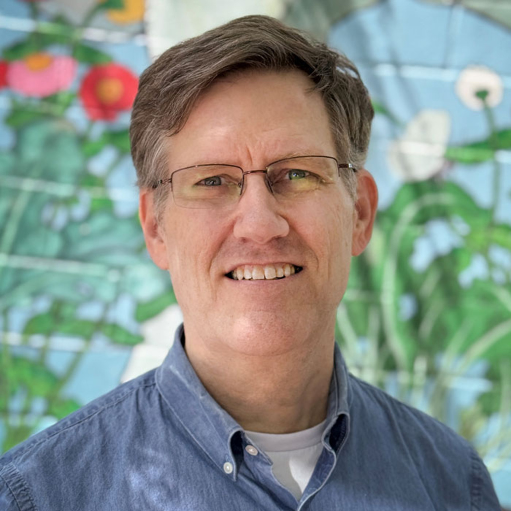 Christopher Liebig smiles for a photo outside in front of a painted floral mural.