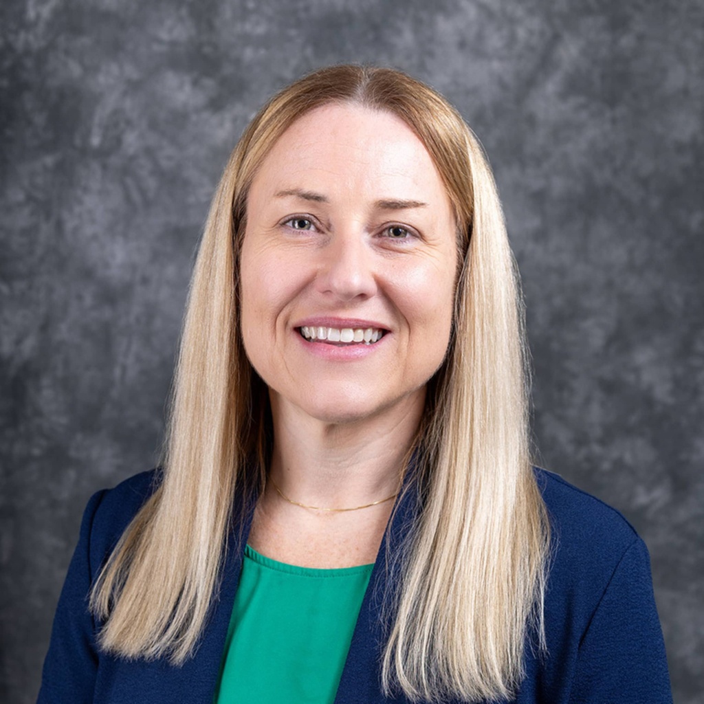 A professional photo of Kara Avis smiling against a mottled, dark gray backdrop.