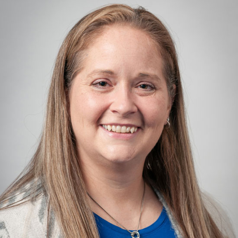 Melissa Plammer, smiling in front of a gray backdrop.