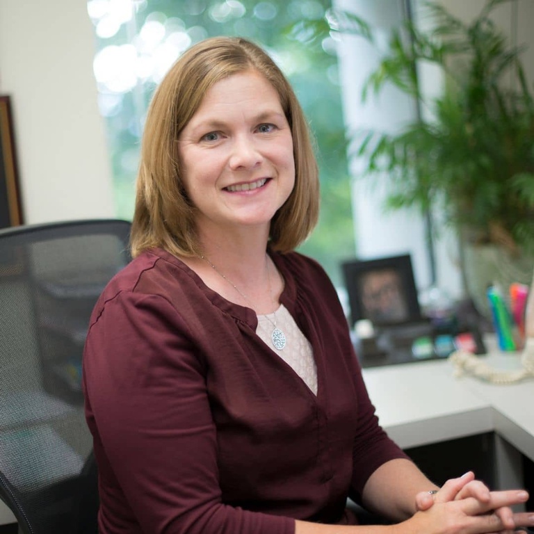 Angie McMullin smiles for a portrait while sitting at her office desk.