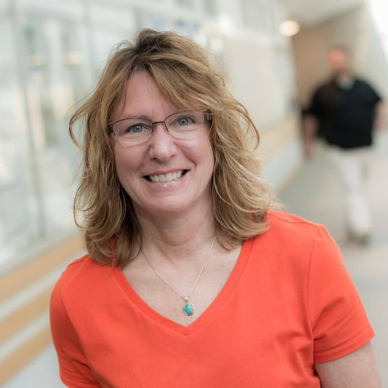 Staff portrait of Julie Kramer smiling in an orange shirt in the hallway of Boyd Law Building.