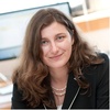 Faculty portrait of Stella Burch Elias, wearing a black blazer and smiling while seated at her desk.