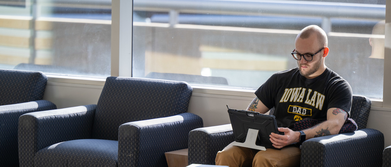 Students sits on main floor of BLB on his laptop by the front windows.