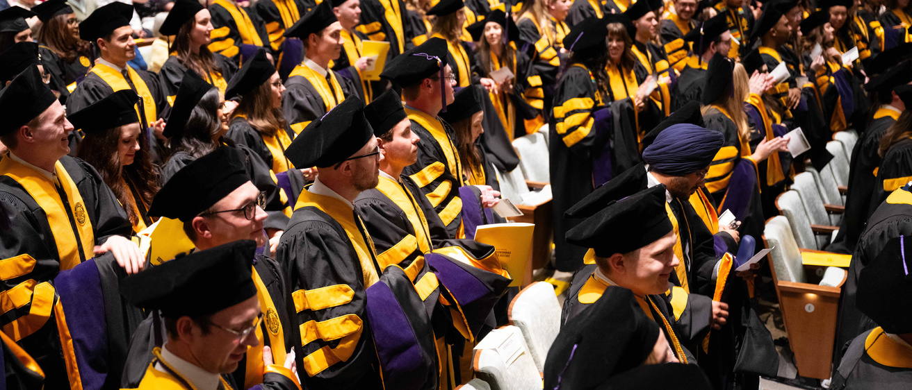 Law graduates stand in Hancher Auditorium. 