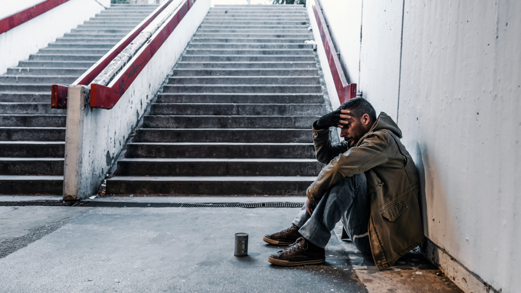 Homeless man sits at the bottom of concrete stairs. 