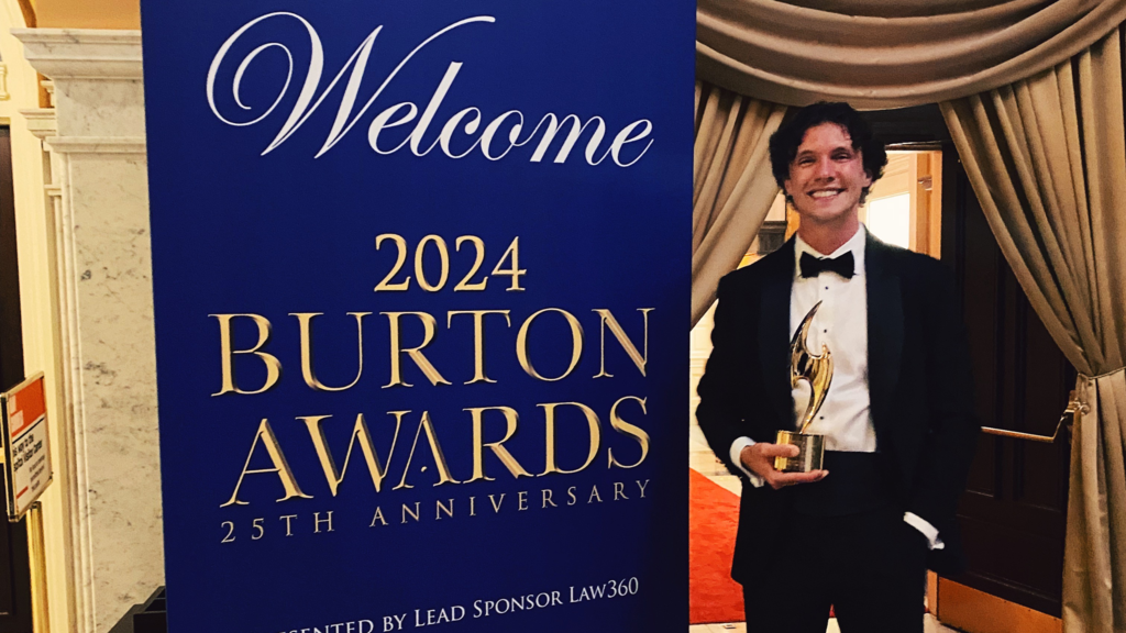 Ben Louviere (23JD) stands in front of Burton Awards sign after winning an award for his legal writing.